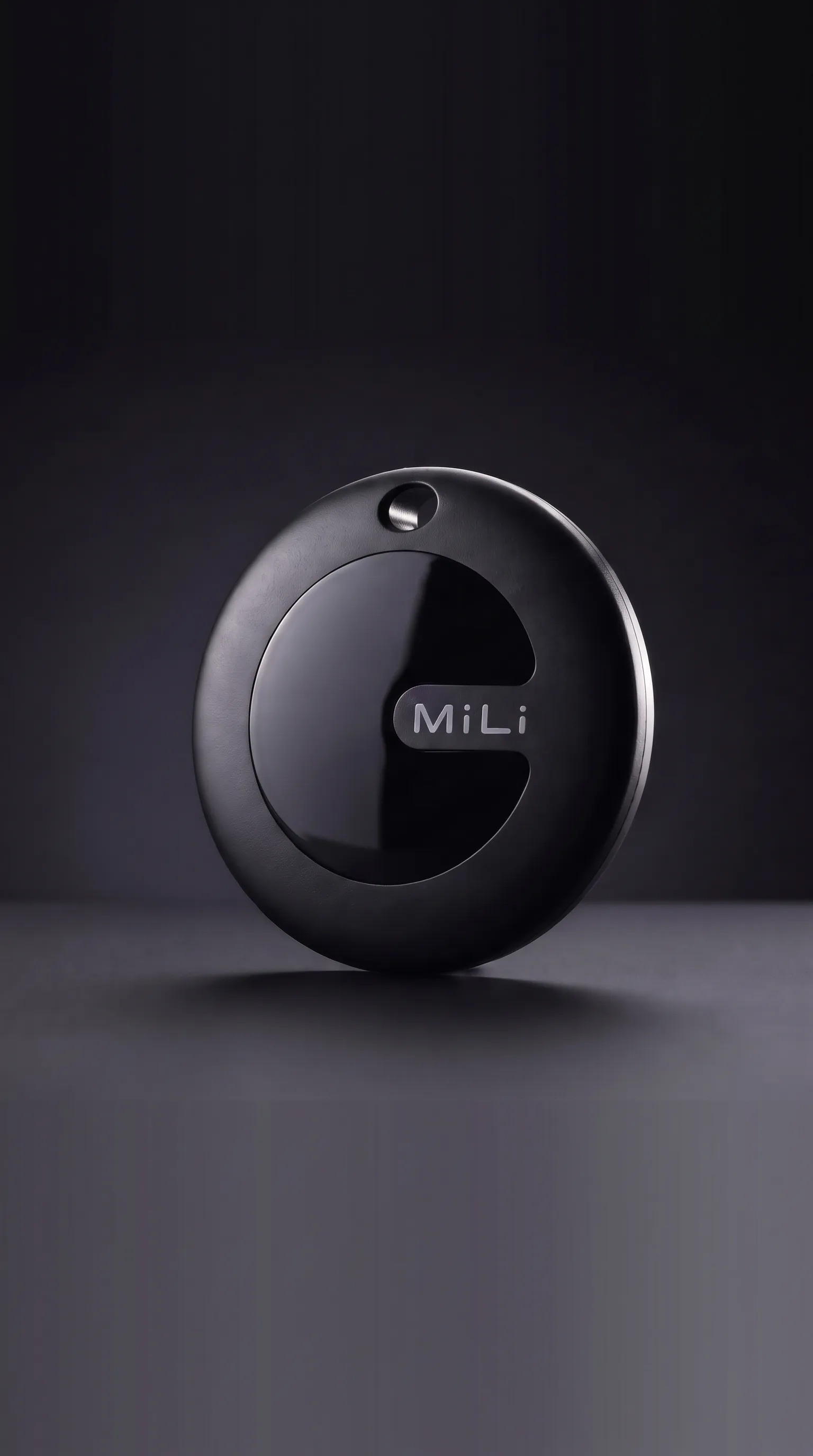 Rastreador MiLi MiTag Duo negro, el disco solo con el logo MiLi en la cara frontal, apoyado de canto sobre una superficie oscura